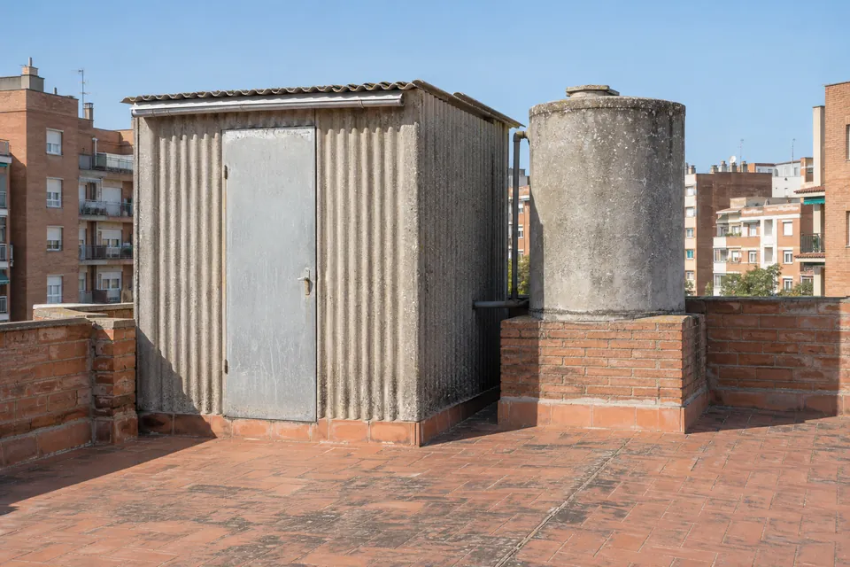 Cubierta ondulada y depósito de agua de fibrocemento antiguos en la azotea de un bloque de pisos