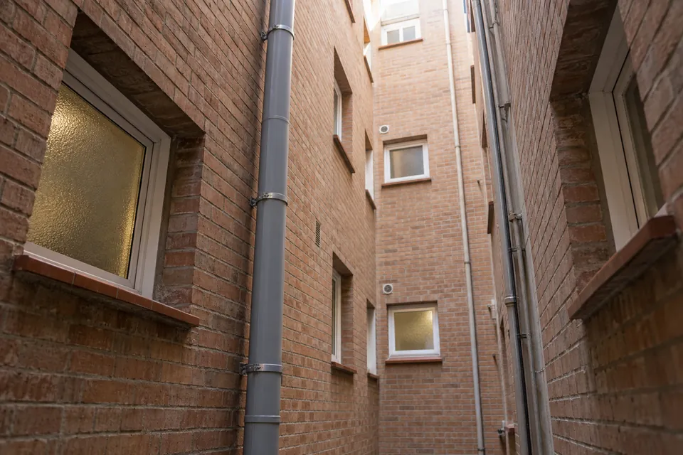 Bajante nueva de PVC gris en el patio de luces de un bloque de pisos de ladrillo