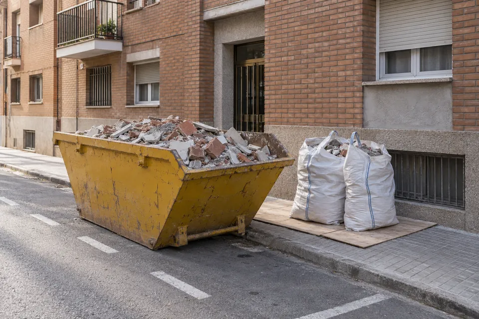 Contenedor de escombros y sacas de obra junto a un bloque de pisos
